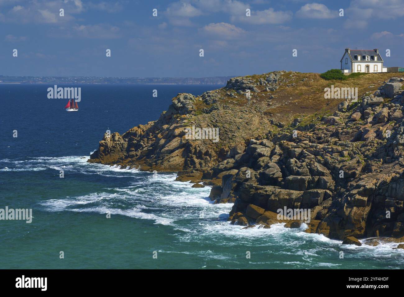 Leuchtturmhaus Phare du Millier auf einer Klippe mit Blick auf das Meer mit Segelschiff unter klarem Himmel, Point du Millier, Beuzec Cap Sizun, Finistere, Britt Stockfoto