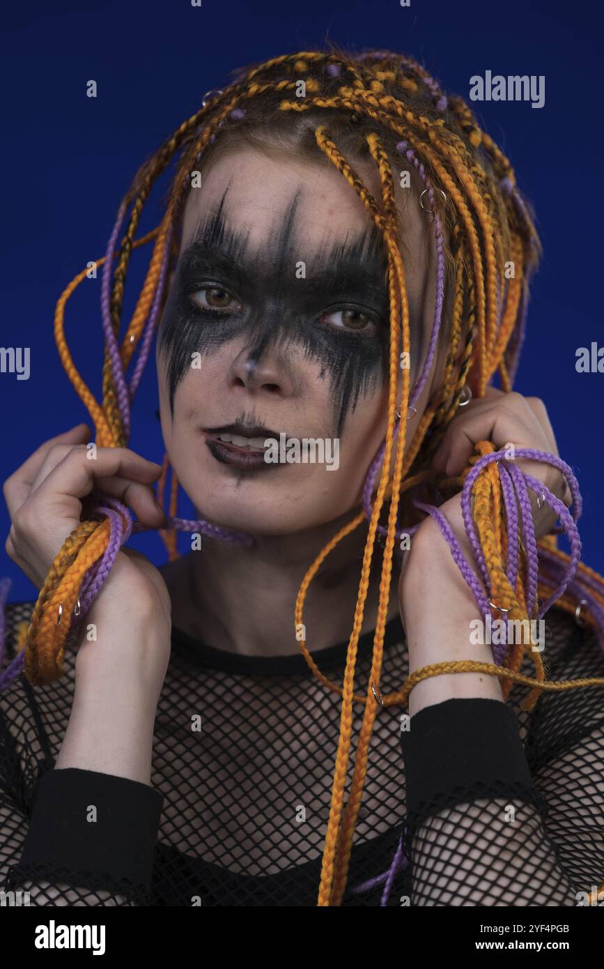 Kinoporträt einer süßen jungen Frau mit orangefarbenem Dreadlocks-Haarschnitt und grauenschwarzem Bühnenschminke auf dem Gesicht. Vorderansicht, Studioaufnahme Stockfoto