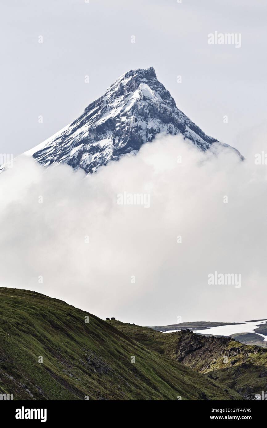 Wunderschöne Berglandschaft der Kamchatka Halbinsel, atemberaubende Aussicht auf den verschneiten Gipfel des Felsenkegels Kamen Vulkan in Wolken. Eurasien, Russischer Fernost, Kamc Stockfoto