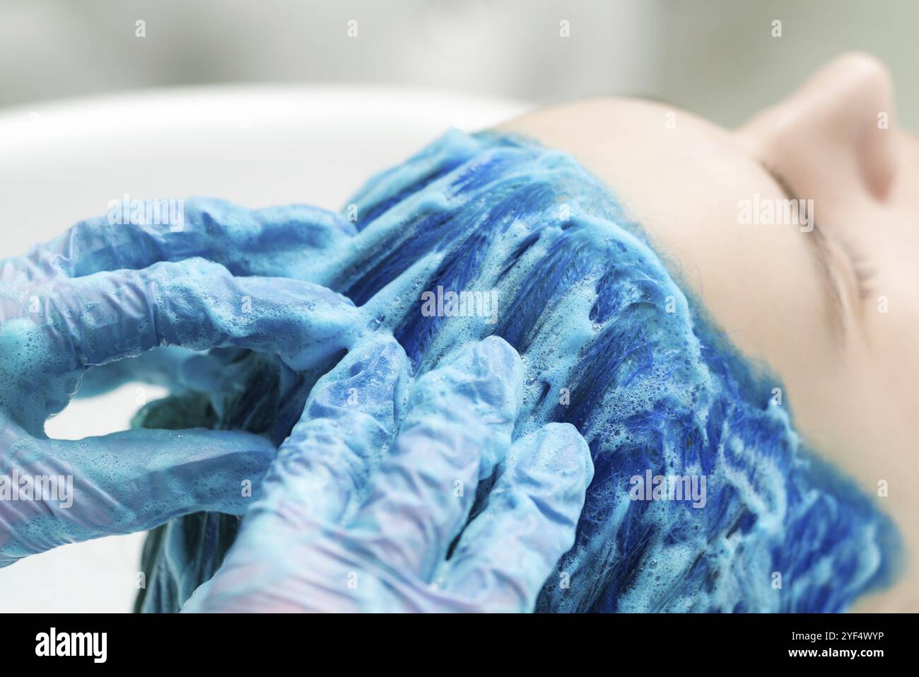 Friseur in Schutzhandschuhen wäscht Kunden blaue Haare mit Shampoo für das Waschen nach dem Prozess der Färbung Haar in schönen Saphir Farbe. Seite V Stockfoto