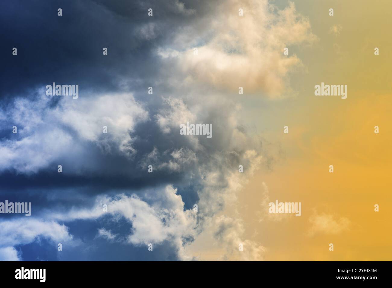 Dramatische blaue Gewitterwolken auf der linken Seite, atemberaubende gelb-goldene flauschige Wolken, die von Sonnenstrahlen auf der rechten Seite beleuchtet werden. Fantastische Aussicht natürliche Meteorologie Backgr Stockfoto