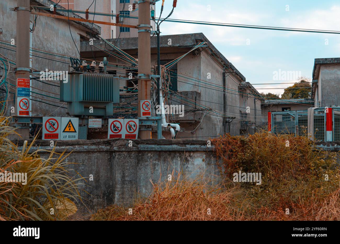 Industriekraftwerk mit mehreren Warnschildern, elektrischen Transformatoren und freiliegenden Kabeln in städtischer Umgebung Stockfoto