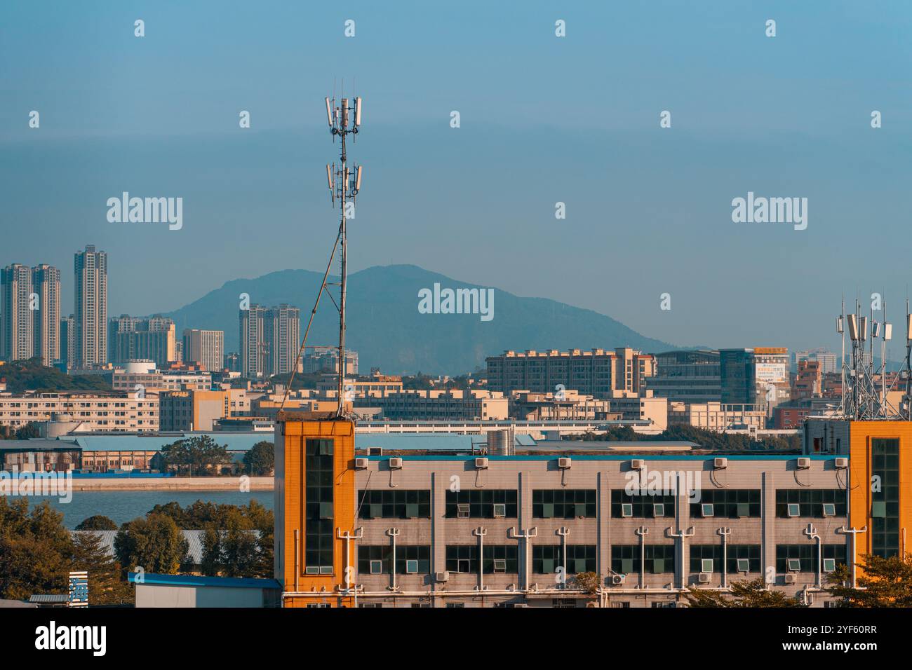 Städtische Skyline mit Telekommunikationstürmen und Bürogebäuden vor einem fernen Bergmassiv unter einem klaren blauen Himmel Stockfoto