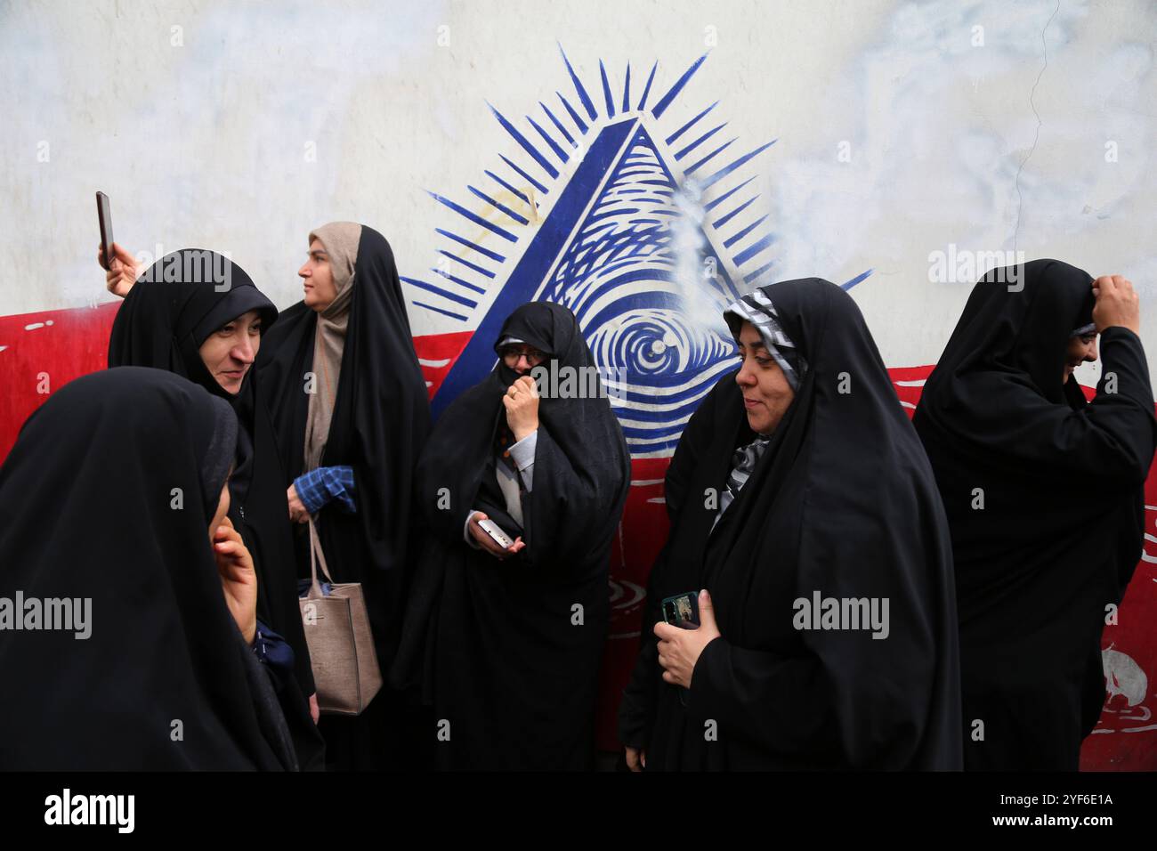 Teheran, Iran. November 2024. Iranische Frauen laufen an einem Wandgemälde entlang der Mauer der ehemaligen US-Botschaft während einer Anti-US-Kundgebung zum 45. Jahrestag der Übernahme durch die US-Botschaft vor dem ehemaligen Botschaftsgebäude vorbei. Am 4. November 1979 übernahmen iranische Studenten die US-Botschaft in Teheran und hielten über 50 amerikanische Diplomaten und Wärter 444 Tage lang als Geiseln. Diese Aktion folgte der Entscheidung der USA, dem entlassenen Schah aus dem Iran die medizinische Behandlung in Amerika zu erlauben. Vor kurzem, am 2. November, warnte der Oberste Führer Ayatollah Ali Khamenei vor einer ernsten Reaktion auf die USA und Israel Stockfoto