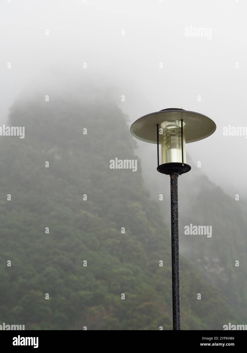 Ein einsamer Leuchtenpfosten steht vor einem nebeligen Berghintergrund, der eine Aura von Ruhe und Introspektion ausstrahlt und die sanfte Beleuchtung die Atmosphäre verbessert Stockfoto