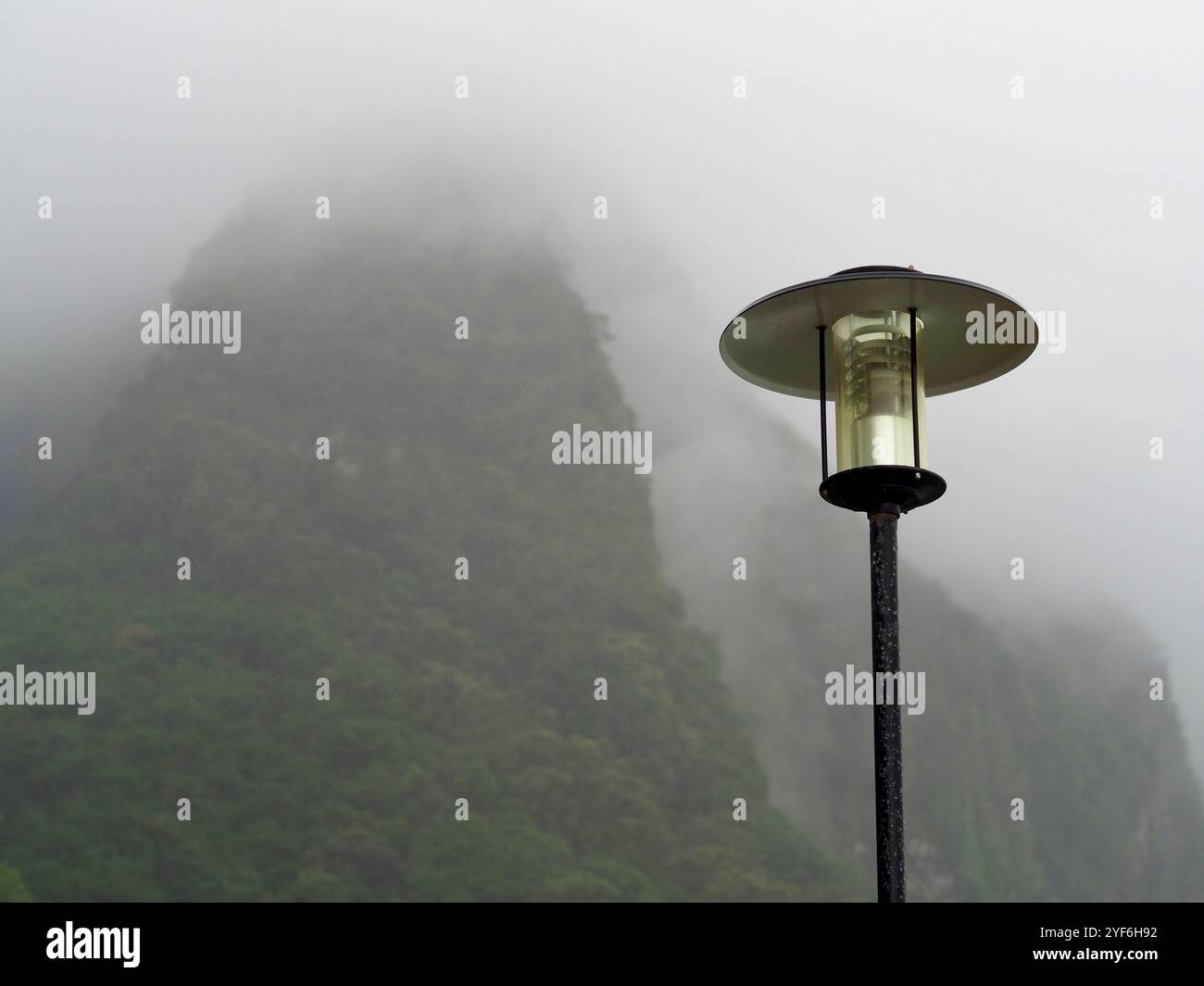 Ein einsamer Leuchtenpfosten steht vor einem nebeligen Berghintergrund, der eine Aura von Ruhe und Introspektion ausstrahlt und die sanfte Beleuchtung die Atmosphäre verbessert Stockfoto