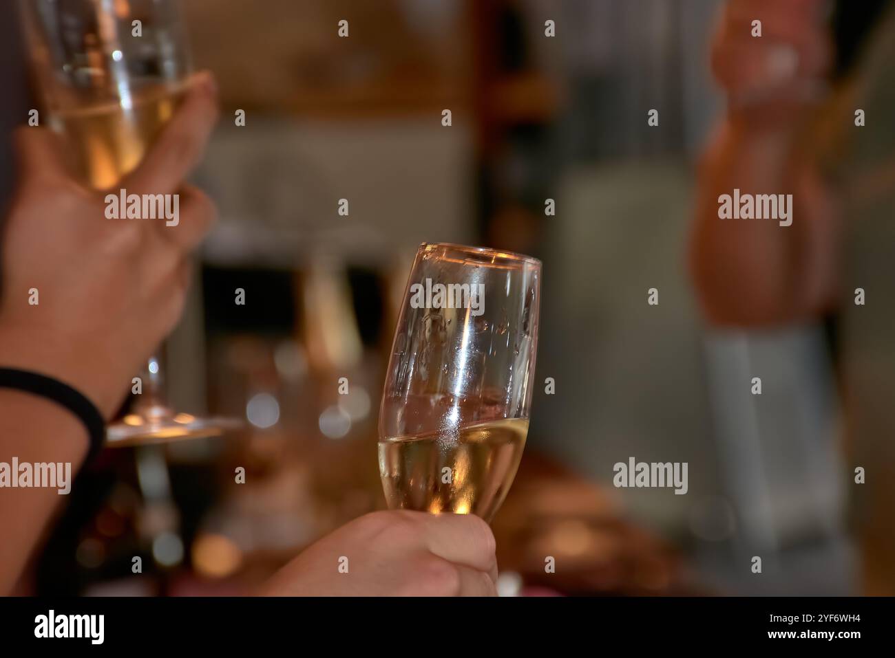 Eine Nahaufnahme der Hände, die während eines Toastes Champagner halten, um einen festlichen Moment festzuhalten. Ideal für Urlaubs-, Party- und Freundschaftsthemen. Stockfoto