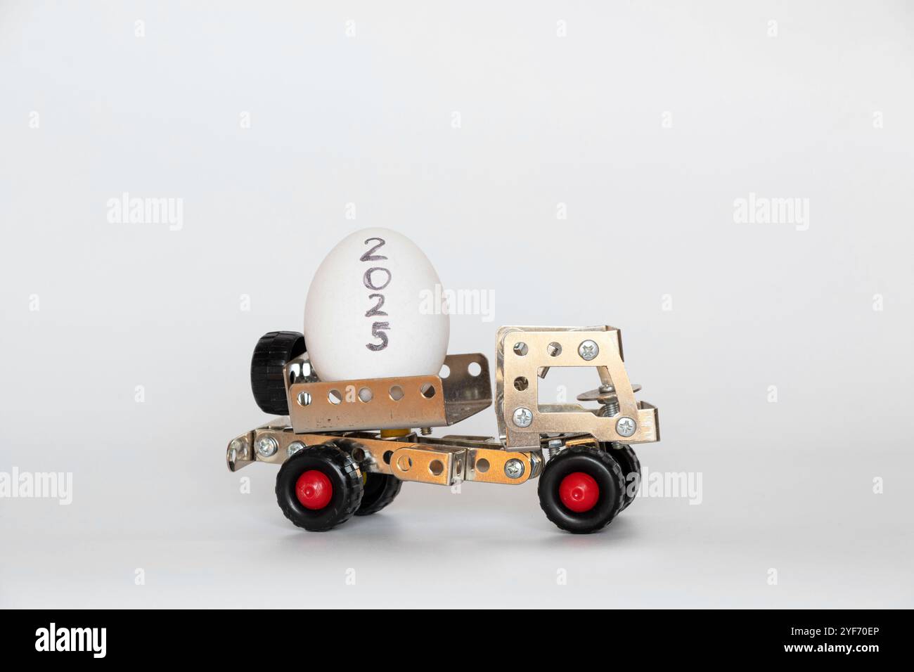 Kinderwagen aus Metall-Bauset transportiert Hühnerei mit Aufschrift 2025 auf weißem Hintergrund, Lebensmittellieferung und Transport Stockfoto