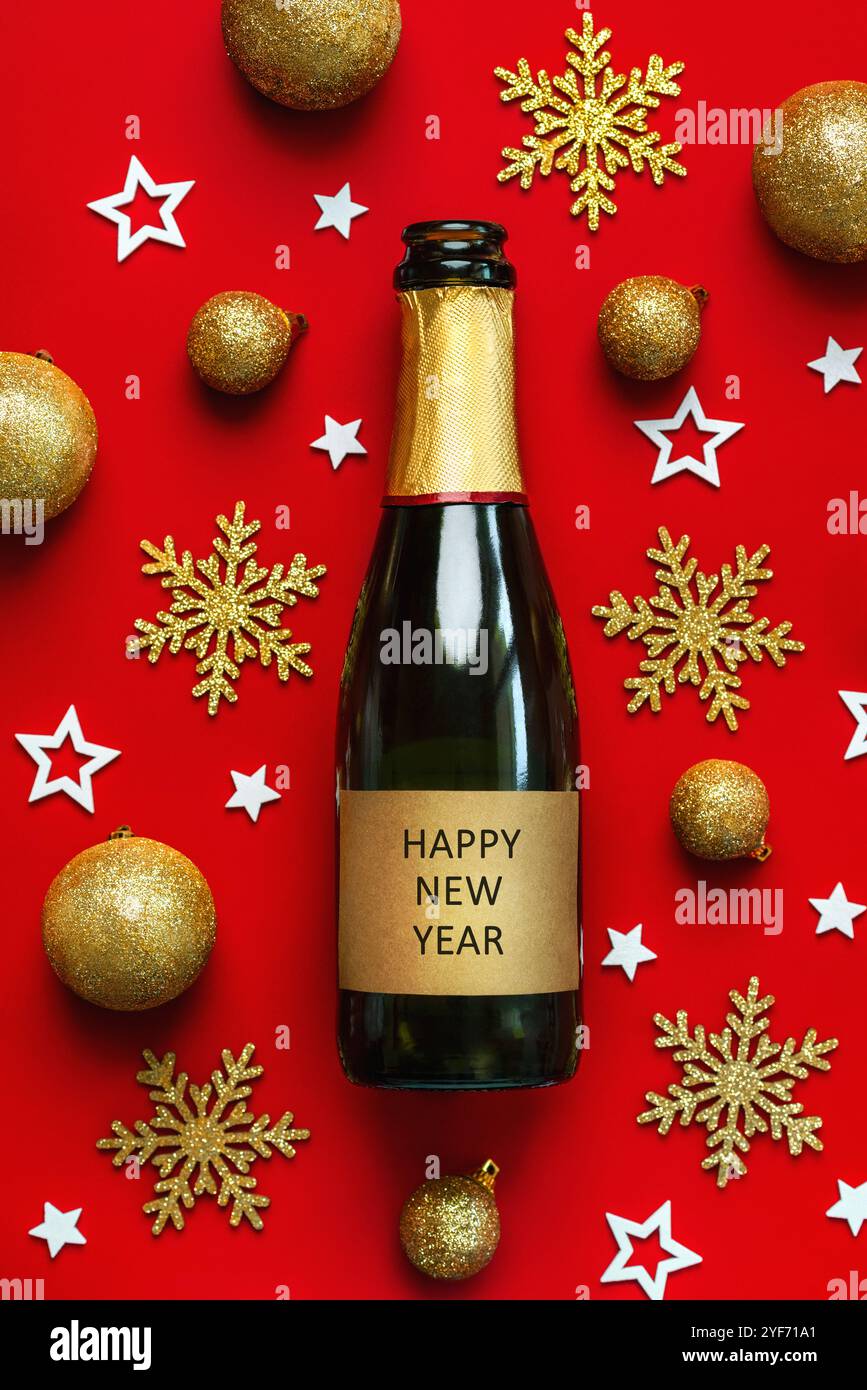 Frohes neues Jahr. Blick von oben auf die Champagnerflasche mit einem goldenen Etikett mit dem Text Happy New Year Around Christmas Balls and Stars auf rotem Hintergrund. Ne Stockfoto