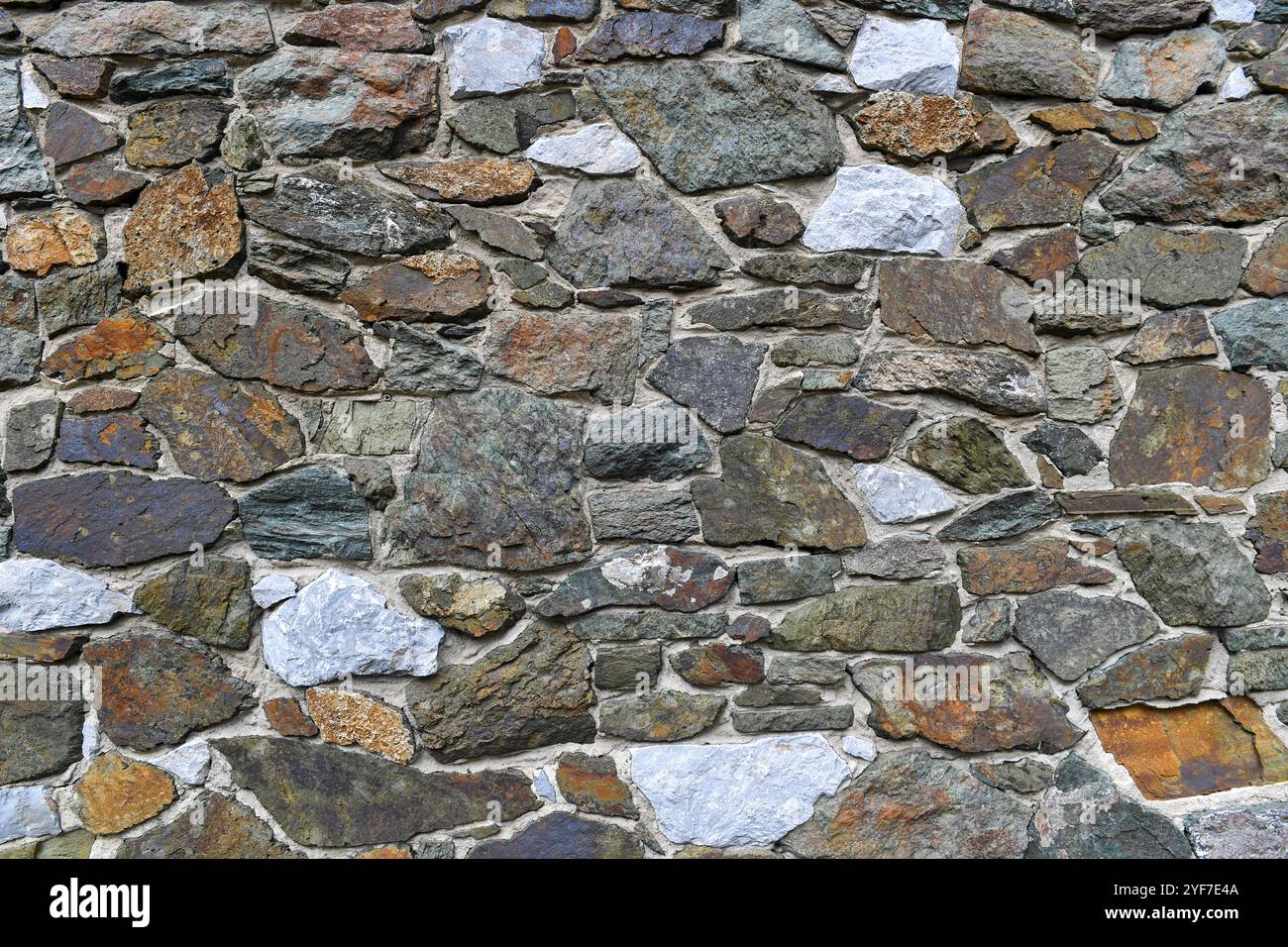 Aus nächster Nähe sehen Sie eine rustikale Steinmauer, die aus unterschiedlich geformten und farbigen Felsen besteht und eine raue und strukturierte Oberfläche mit natürlichen Farbtönen zeigt Stockfoto