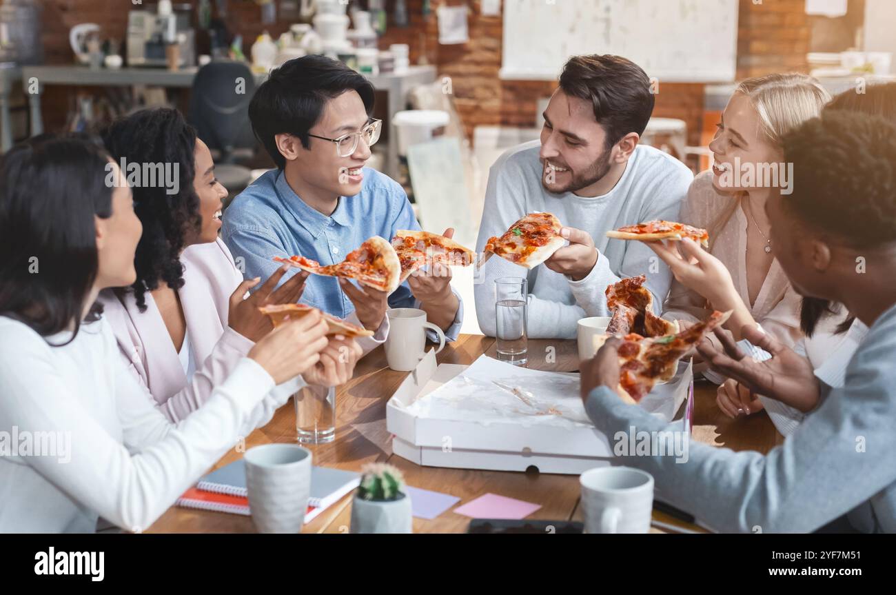 Freundliches internationales Team, das gemeinsam Pizza im Büro genießt Stockfoto