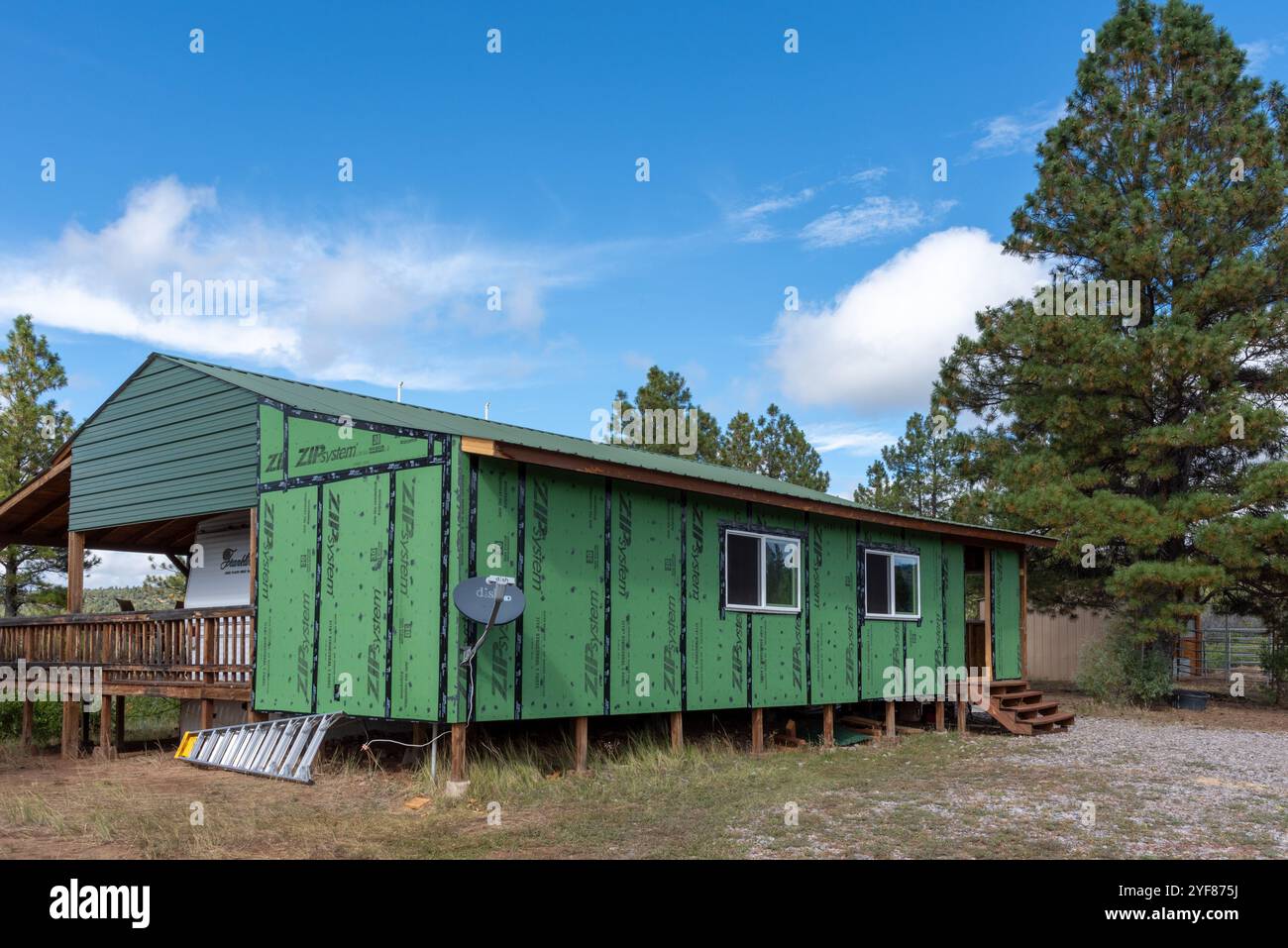 Struktur im Bau, einschließend dauerhaft geparkten Reiseanhänger, mit grüner wetterfester Wandummantelung, Nord-New Mexico, USA. Stockfoto