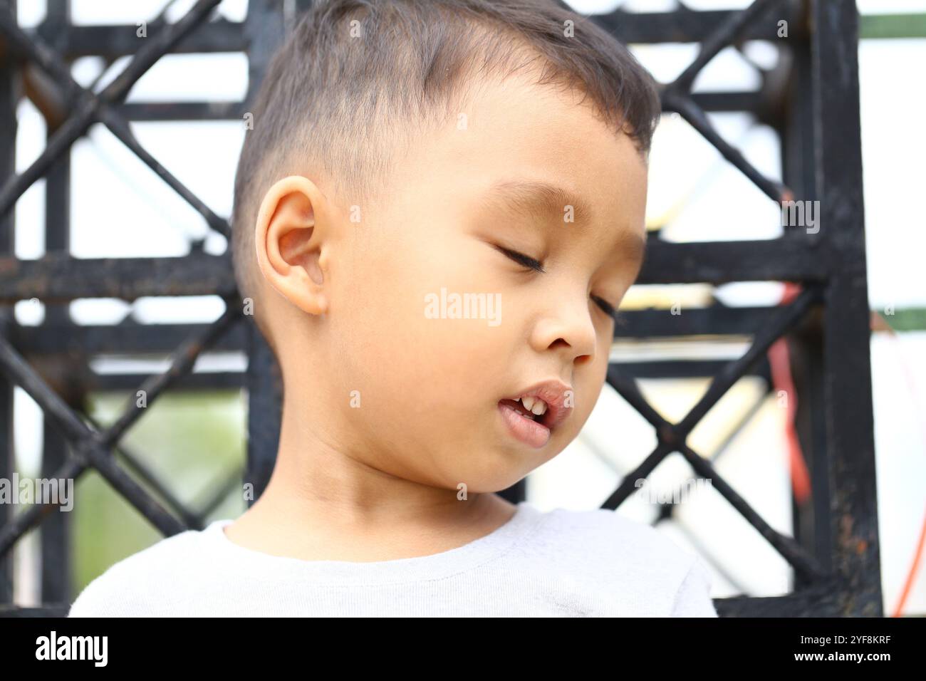 Ein ehrliches Porträt eines nachdenklichen Kindes mit geschlossenen Augen, das einen Moment der Gelassenheit und Unschuld festhält. Dieses Bild spiegelt kindliches Wunder und Imagi wider Stockfoto