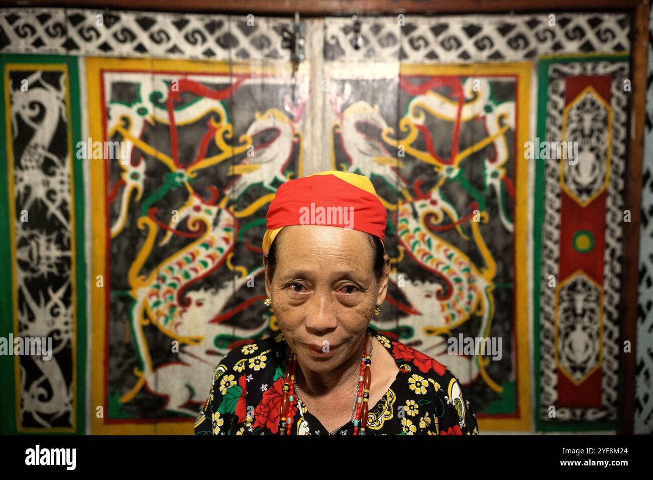 Porträt einer Frau in einem Hintergrund traditioneller Wandmalerei im Bali Gundi Langhaus der traditionellen Dayak Taman Gemeinde in Sibau Hulu, Putussibau Utara, Kapuas Hulu, West Kalimantan, Indonesien. Laut Hernan Vales, Leiter der Abteilung für indigene Völker und Minderheiten der Vereinten Nationen, in einer Veröffentlichung des UN-Menschenrechtsbüros des Hohen Kommissars (OHCHR) im September 2024, sind Stimmen indigener Völker entscheidend für die Förderung ihrer Menschenrechte und ihrer Beteiligung an internationalen Entscheidungen. Stockfoto