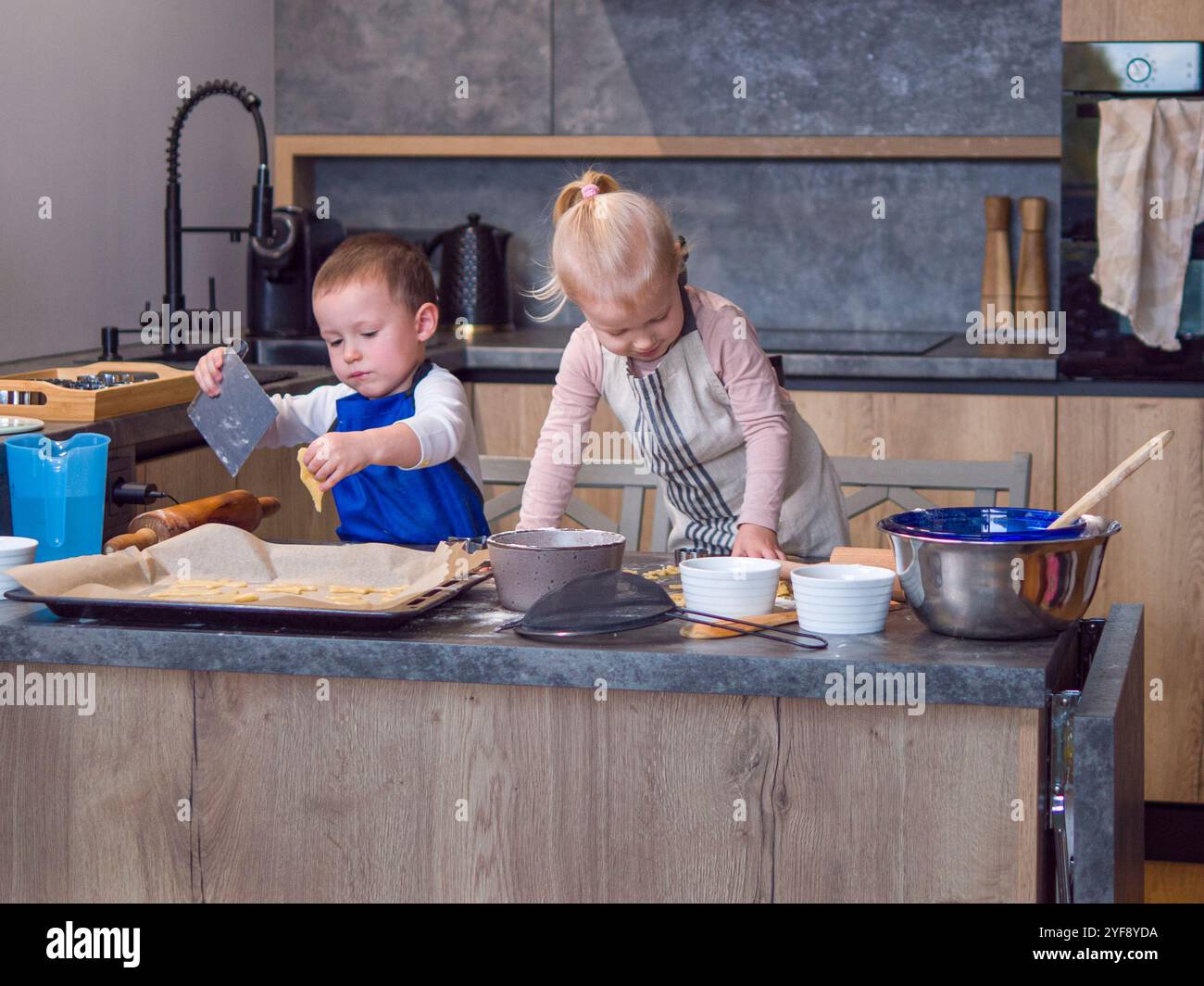 Zwei kleine Kinder, Bruder und Schwester, backen Kekse in der modernen Küche, legen Teig sorgfältig auf Backbleche, die ihre Teamarbeit und Freude machen Stockfoto