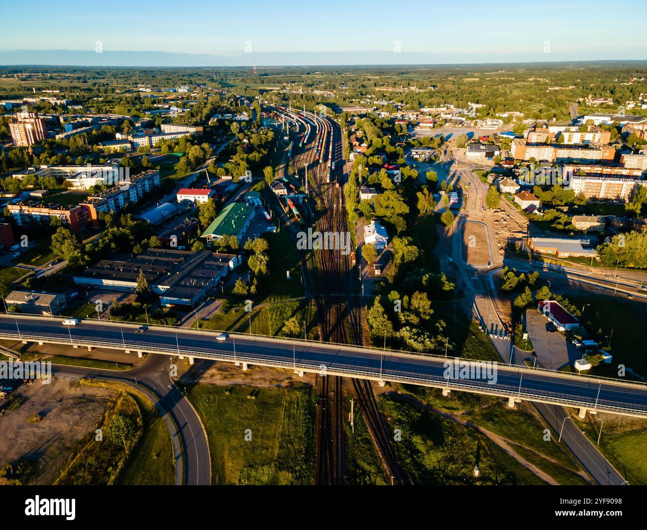 Friedliche urbane Flucht: Grüne Felder treffen auf sonnenbeschienene Straßen und Eisenbahnen in Aerial View Stockfoto