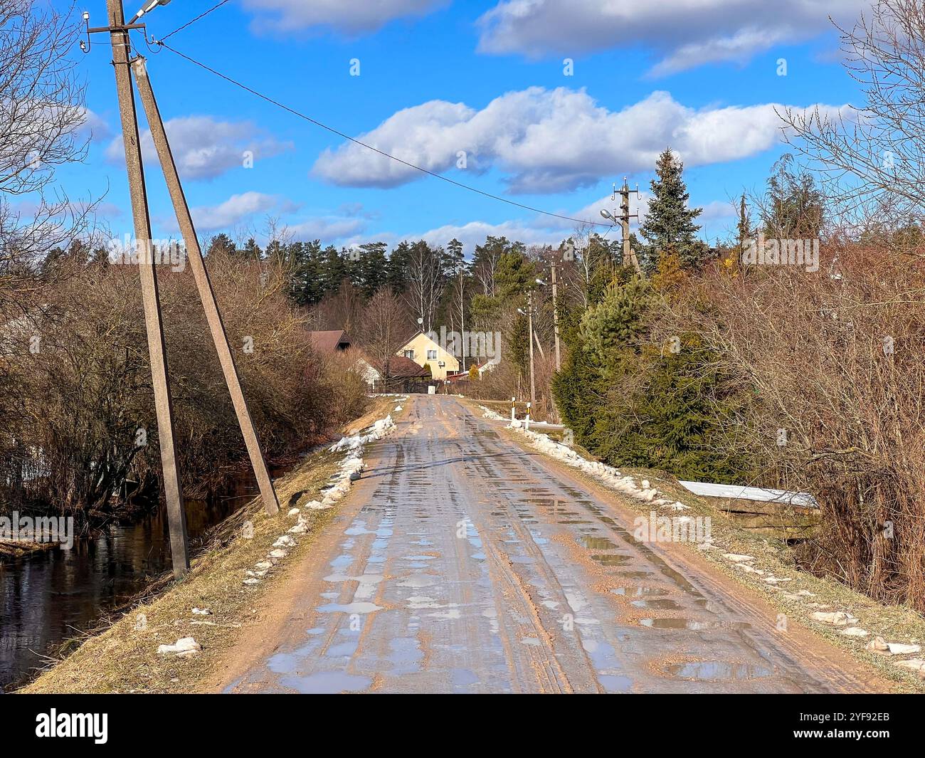 Charmante Country Road mit Pfützen und Schneebesen führt zu einem gemütlichen Dorfhaus Stockfoto