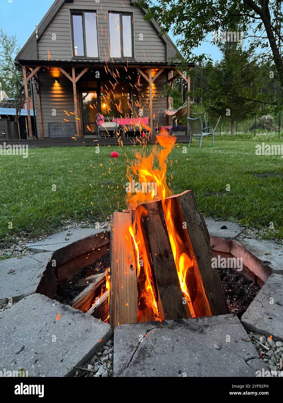 Gemütliches abendliches Lagerfeuer im Hinterhof mit Sparks Flying und privatem Haus dahinter Stockfoto