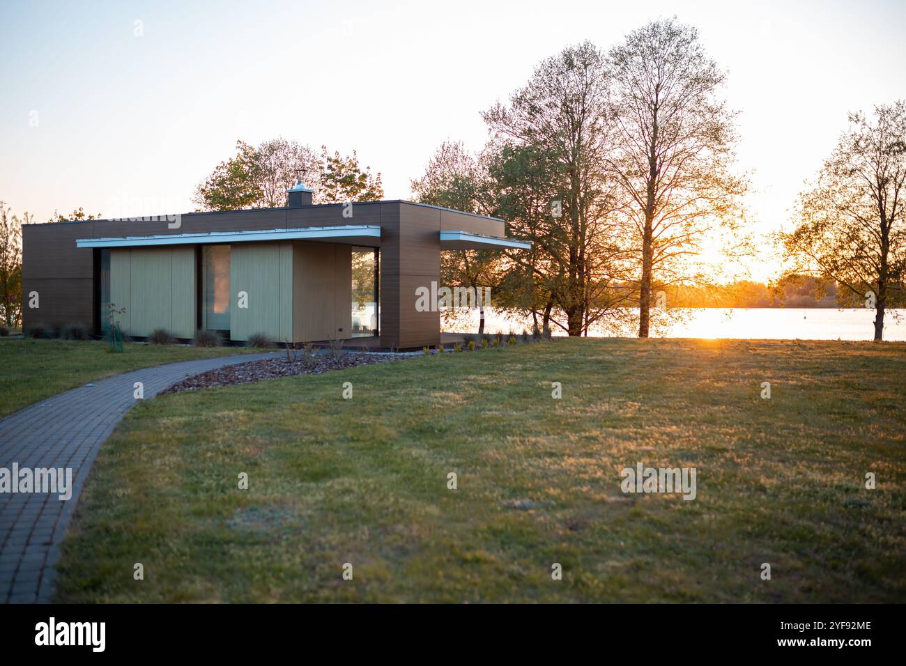 Moderne, minimalistische Architektur eines kleinen Hauses am See, erfasst zur goldenen Stunde mit einem Weg, der zu ihm führt Stockfoto