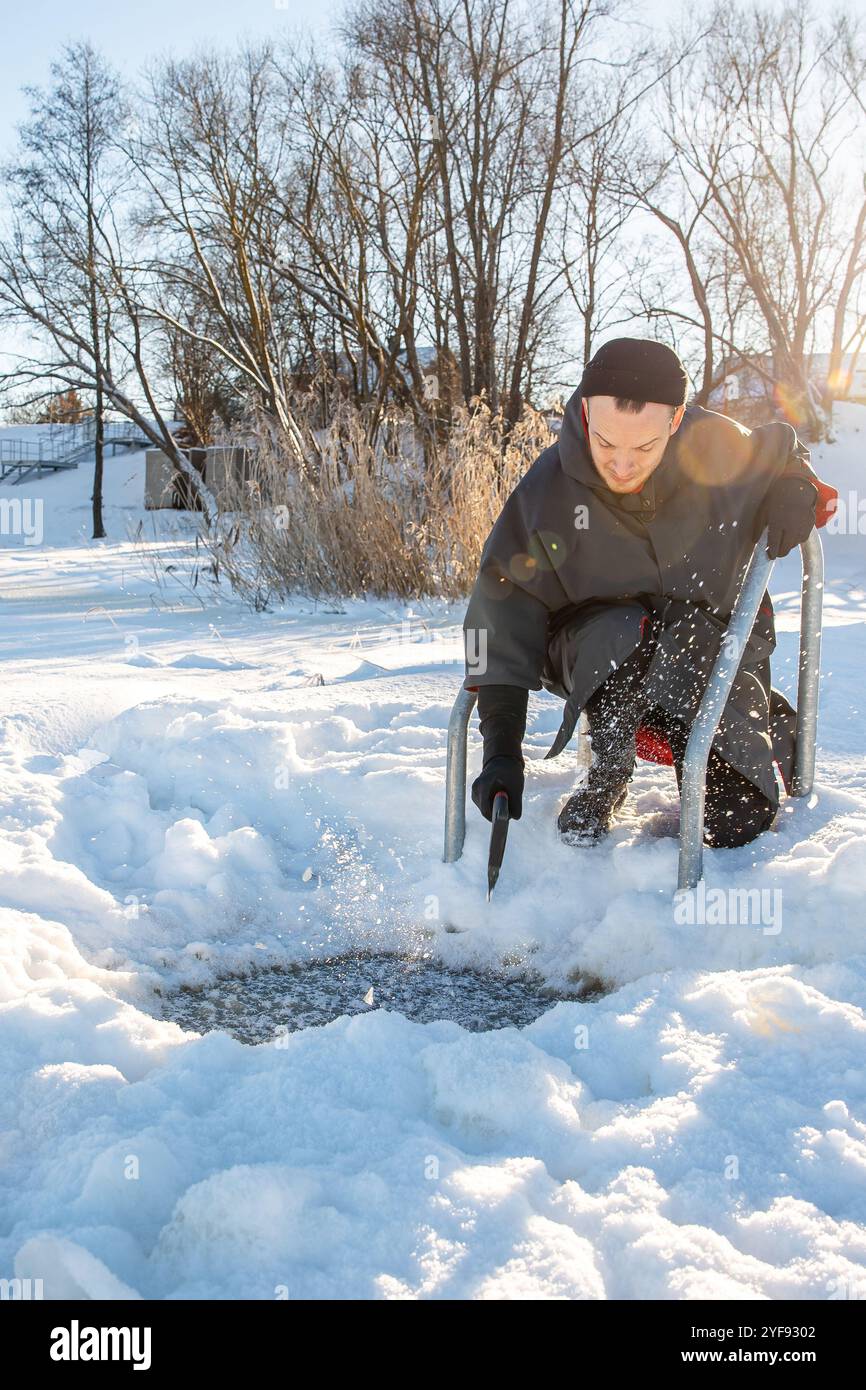 Mann, der ein Loch im Eis mit einer Axt ausgräbt, um an kalten, sonnigen Wintertagen im Winter schwimmen zu können Stockfoto