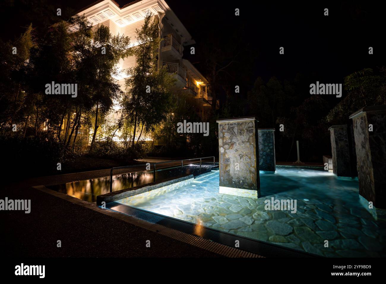 Entspannen Sie sich in einem luxuriösen Touristenresort mit einem wunderschön beleuchteten Swimmingpool, der nachts ein ruhiges Ambiente unter dem Sternenhimmel schafft Stockfoto