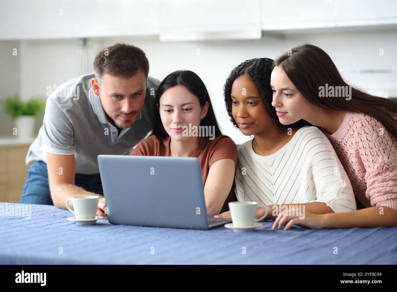 Vier ernsthafte interrassische Freunde, die zusammen in der Küche zu Hause einen Laptop benutzen Stockfoto