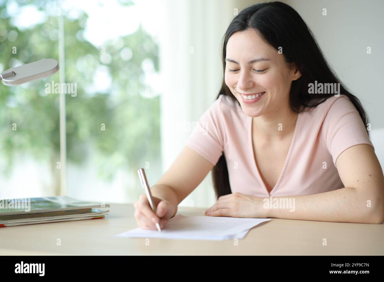 Glückliche asiatische Frau, die zu Hause ein Formular ausfüllt oder einen Vertrag unterschreibt Stockfoto