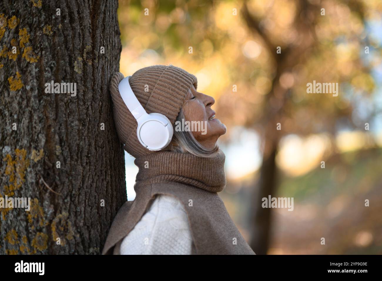 Porträt einer schönen Seniorin mit Kopfhörern im Herbstpark, die Musik mit geschlossenen Augen hört. Stockfoto