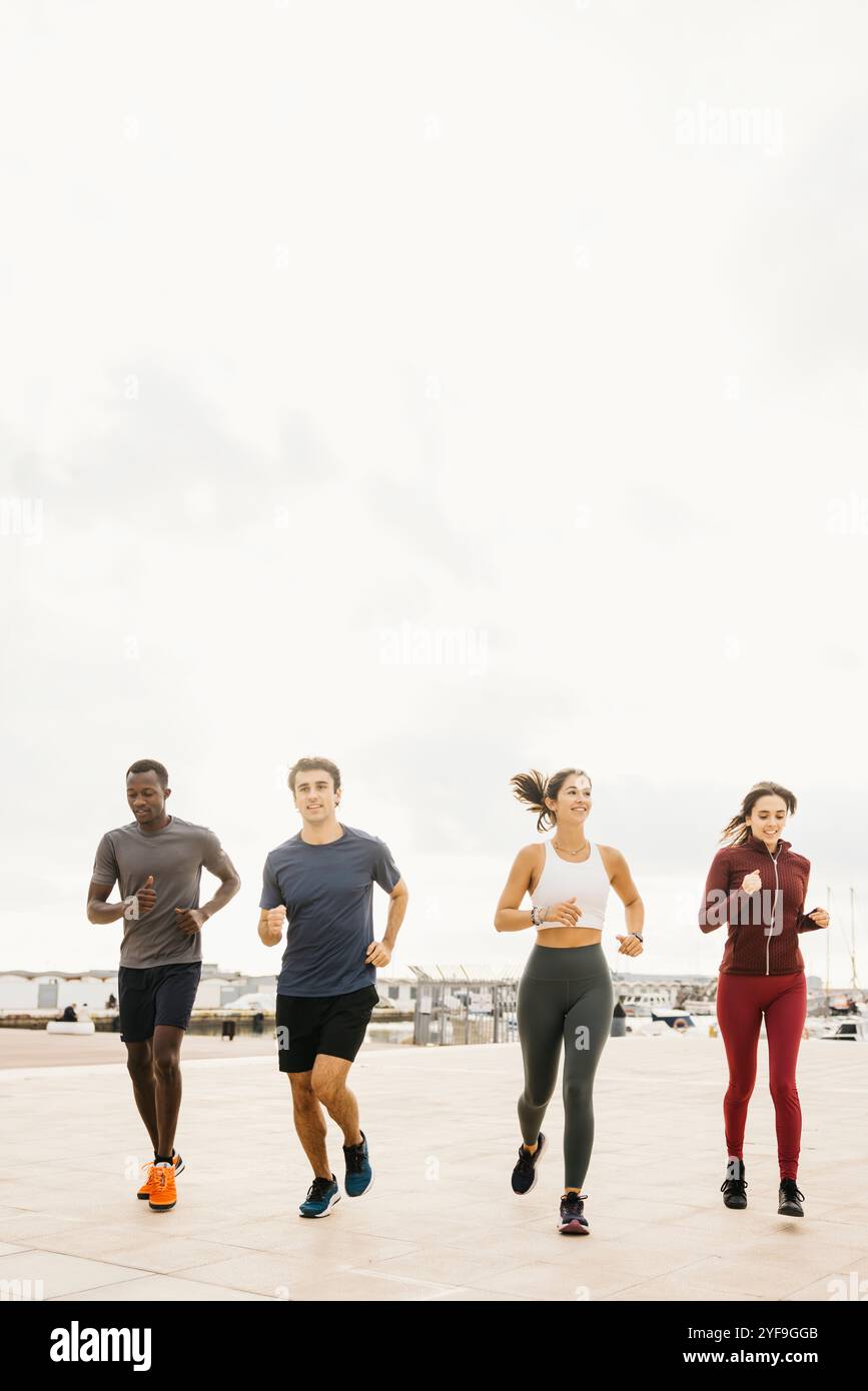 Eine bunte Gruppe von Freunden genießt einen morgendlichen Jog am Meer und fördert durch Outdoor-Übungen einen gesunden Lebensstil und eine Fitness-Motivation. Stockfoto
