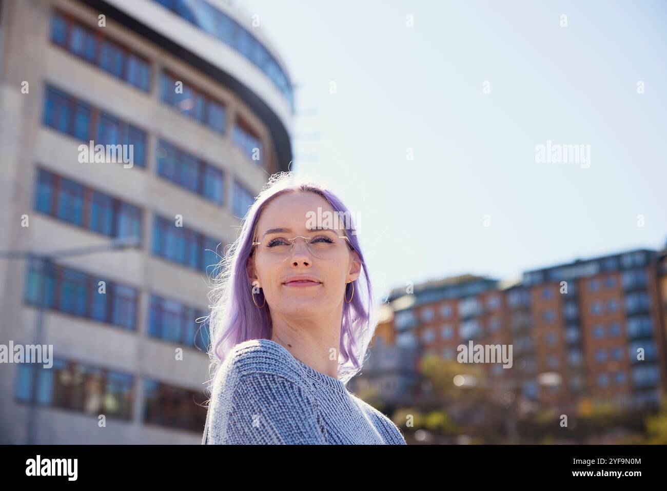 Lächelnde junge Frau mit gefärbtem Haar, die eine Brille trägt und am sonnigen Tag wegschaut Stockfoto