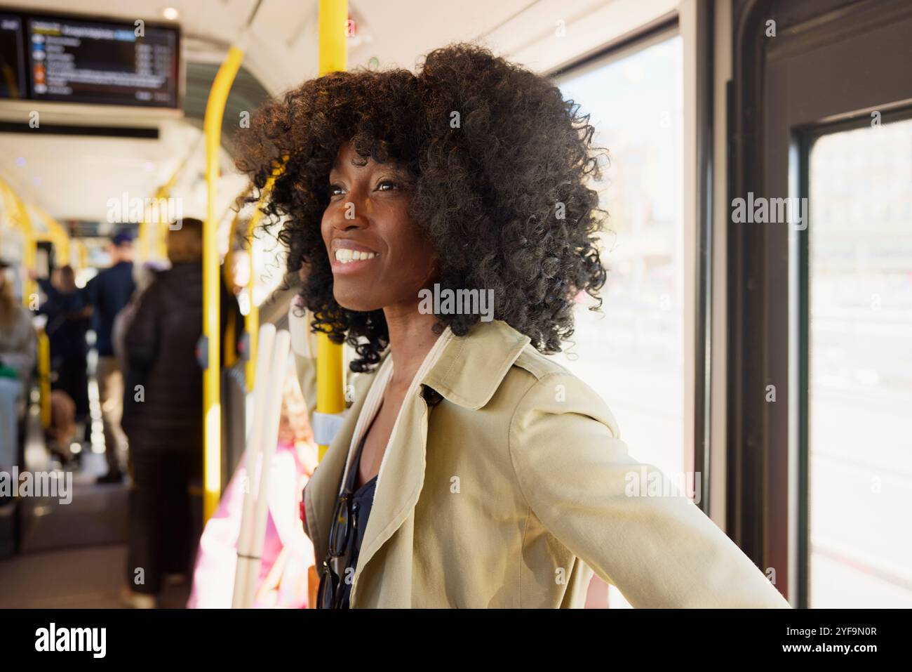 Lächelnde junge Frau mit lockigen Haaren, die wegschaut, während sie im Bus reist Stockfoto