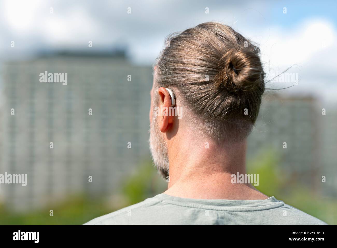 Rückansicht eines Menschen in Haarbrötchen mit Hörgerät Stockfoto