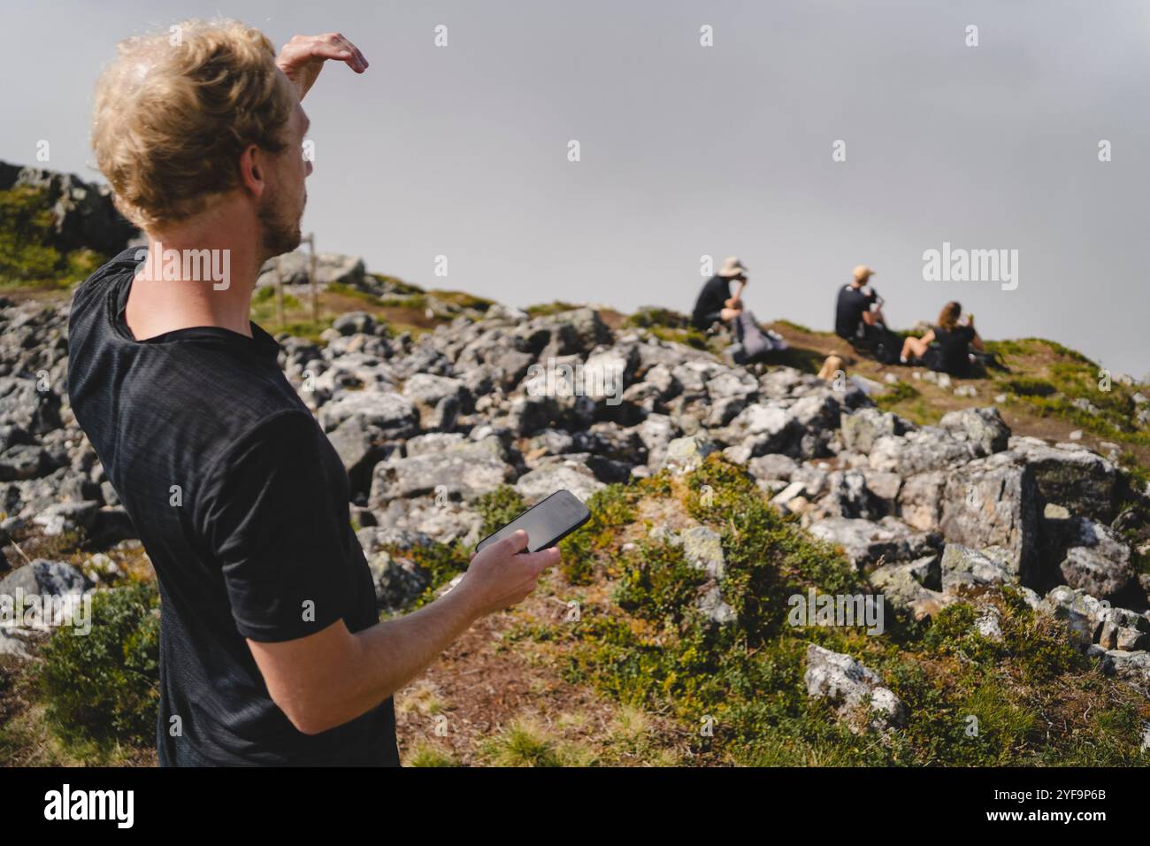Mittelgroßer Mann, der das Telefon hält, während er auf dem Berg vor klarem Himmel steht Stockfoto