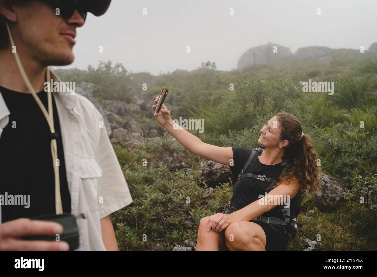 Mittelteil eines jungen Mannes mit einer Freundin, die während des Wanderns Selfie im Hintergrund macht Stockfoto