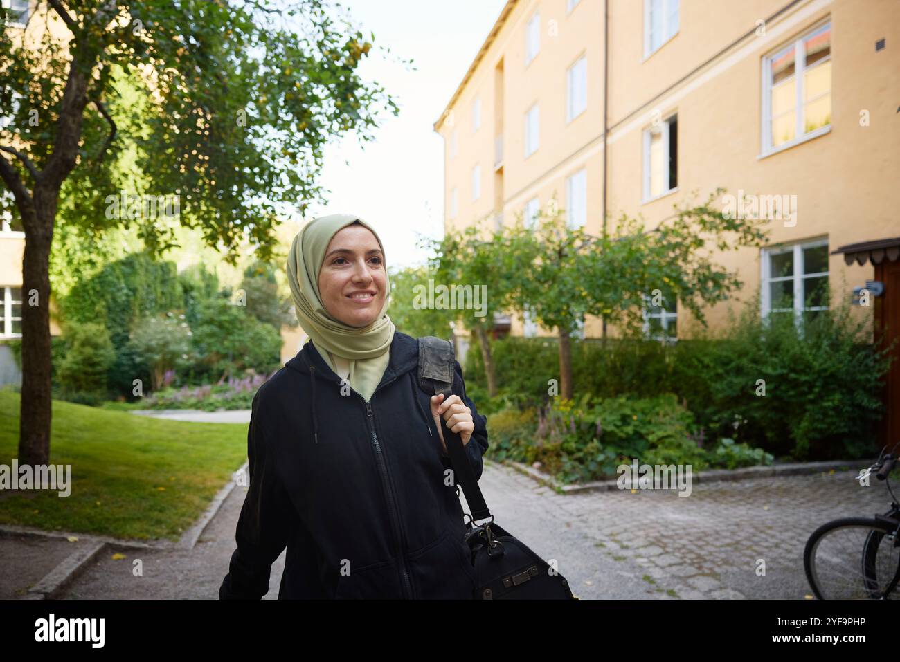 Glückliche Frau, die einen Hijab trägt, während sie auf einem Fußweg vor dem Gebäude läuft Stockfoto