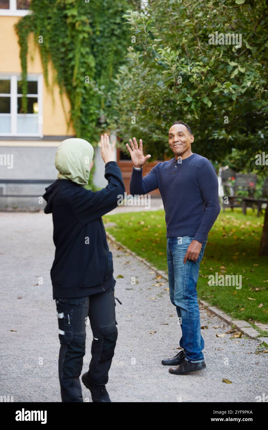 Lächelnde, reife Hand winkelt weibliche Nachbarin, während sie auf dem Fußweg im Garten steht Stockfoto