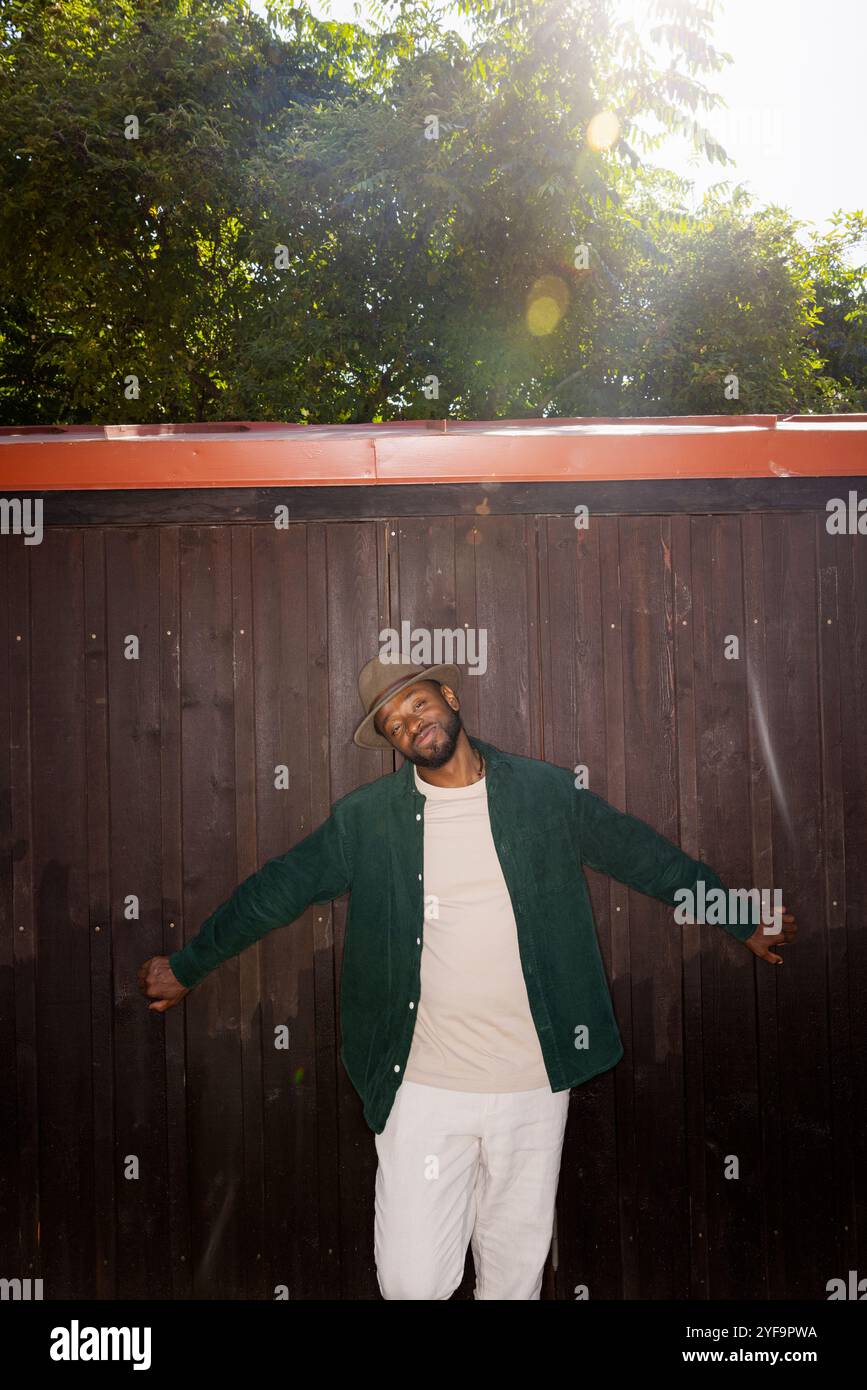 Modischer junger Mann, der an sonnigen Tagen an einer braunen Wand steht Stockfoto