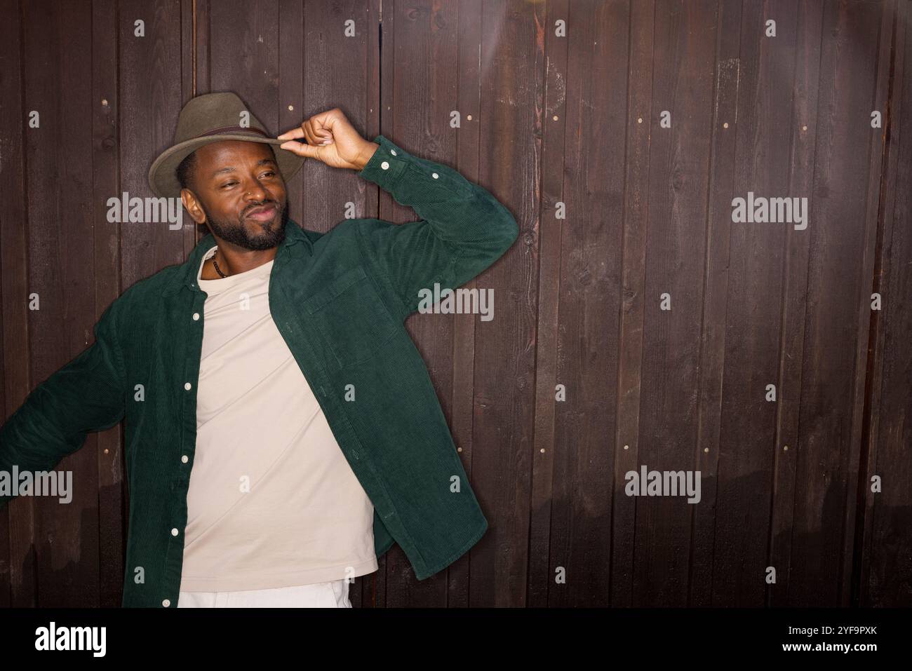 Lächelnder junger Mann, der einen Hut gegen die braune Wand wirft Stockfoto