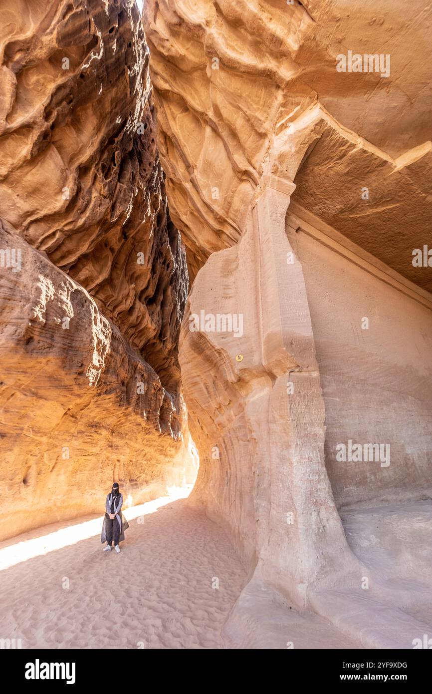 AL ULA, SAUDI-ARABIEN - 9. NOVEMBER 2021: Ortskundiger Reiseleiter in der engen Passage durch den Berg Jabal Ithlib, den Siq, neben dem Diwan, in Felsen gehauene Kammer, Stockfoto