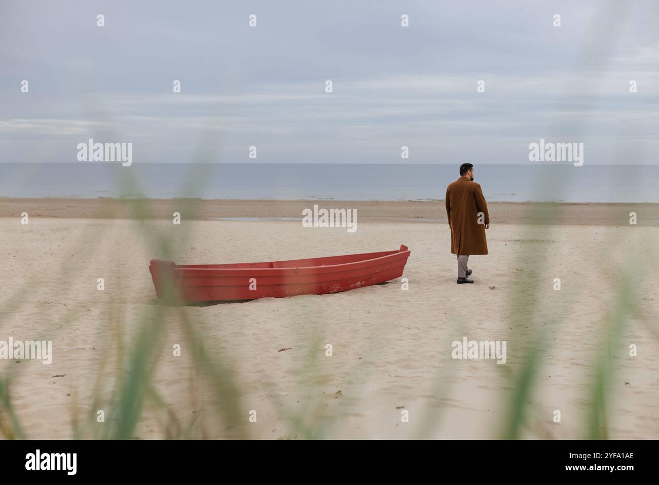 Hübscher junger Erwachsener, der mit rotem Boot an einem Strand spaziert Stockfoto