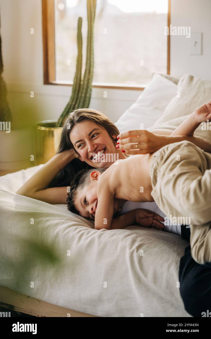 Mutter und Sohn kuscheln sich fröhlich in einem gemütlichen Bett am Fenster Stockfoto