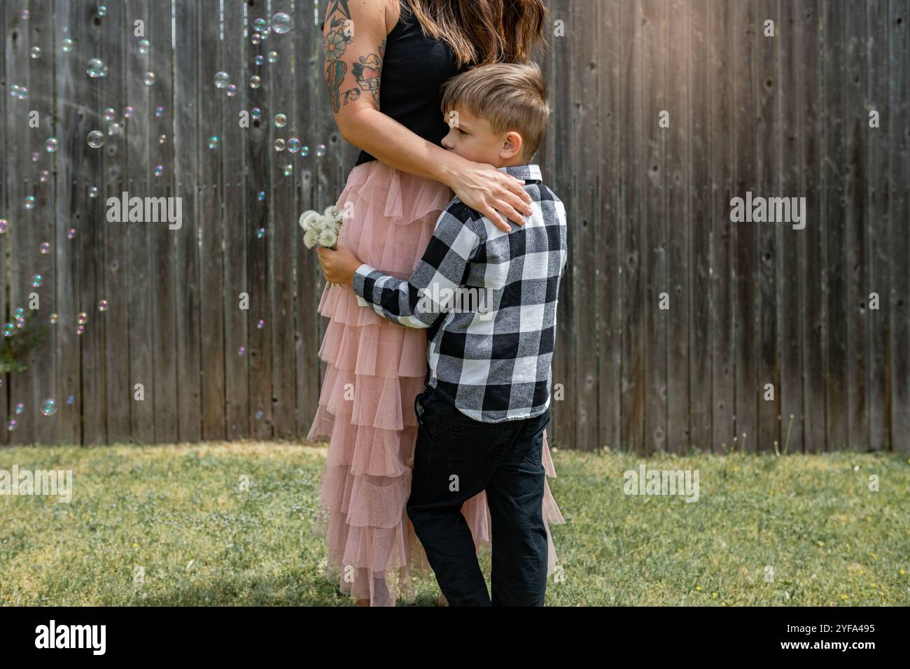 Mutter und Sohn stehen und umarmen draußen mit Blasen und Sonnenschein Stockfoto