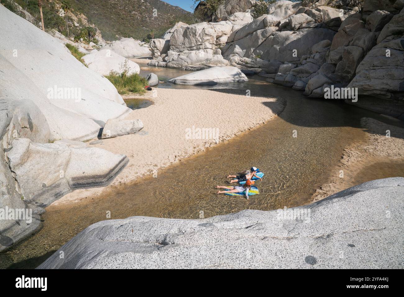 Ein Junge und ein Mädchen schweben auf Boogie Boards in einem flachen Bach Stockfoto