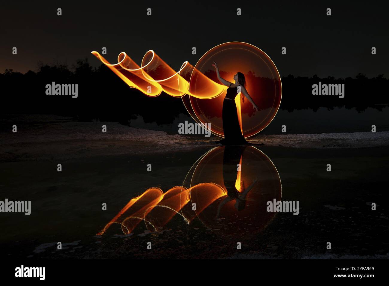 Frau posiert für Lichtmalerei Fotos mit hellen Lichtern in der Dunkelheit. Reflexion im Wasser Stockfoto