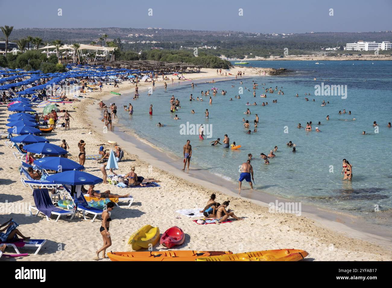 PROTARAS, ZYPERN, 7. August 2020: Touristen schwimmen im türkisfarbenen Meerwasser, entspannen und Sonnenbaden unter Sonnenschirmen während der Sommerferien Stockfoto