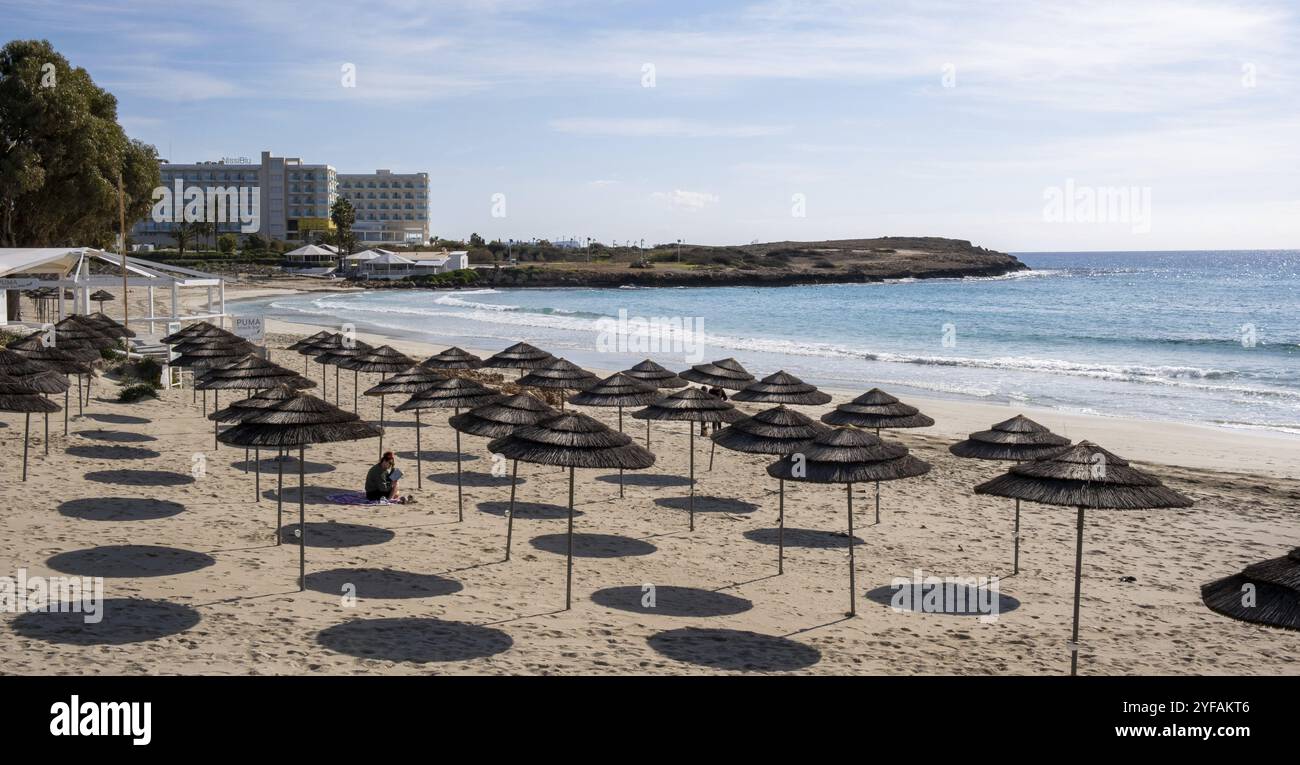 Protaras, Zypern, 29. Januar 2023: Frau liest ein Buch am Sandstrand im Winter unter Sonnenschirmen. Menschen, die im Freien aktiv sind. Gesunder Lebensstil, Stockfoto