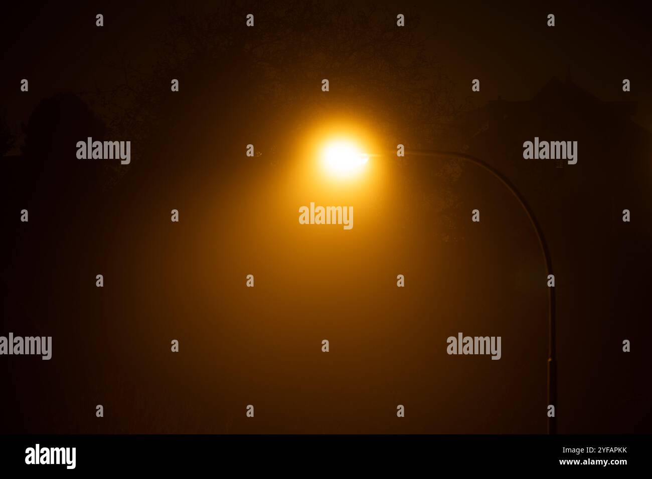 Orangefarbenes Straßenlaternenlicht, das nachts durch dicken Herbstnebel schneidet. Erhöhter Aussichtspunkt, diffuses Licht, stimmungsvolle Atmosphäre, keine Leute. Stockfoto