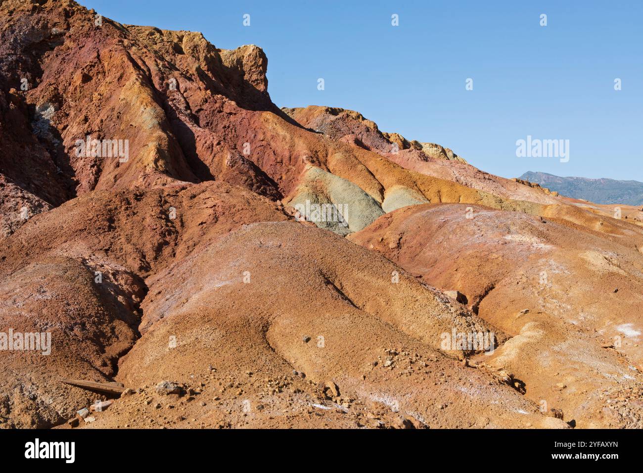 Erodierte, mineralbefleckte Hügel in der verlassenen Mine Mazarrón, Murcia, mit sattem Rost, Orange und Erdtönen unter einem klaren blauen Himmel. Stockfoto