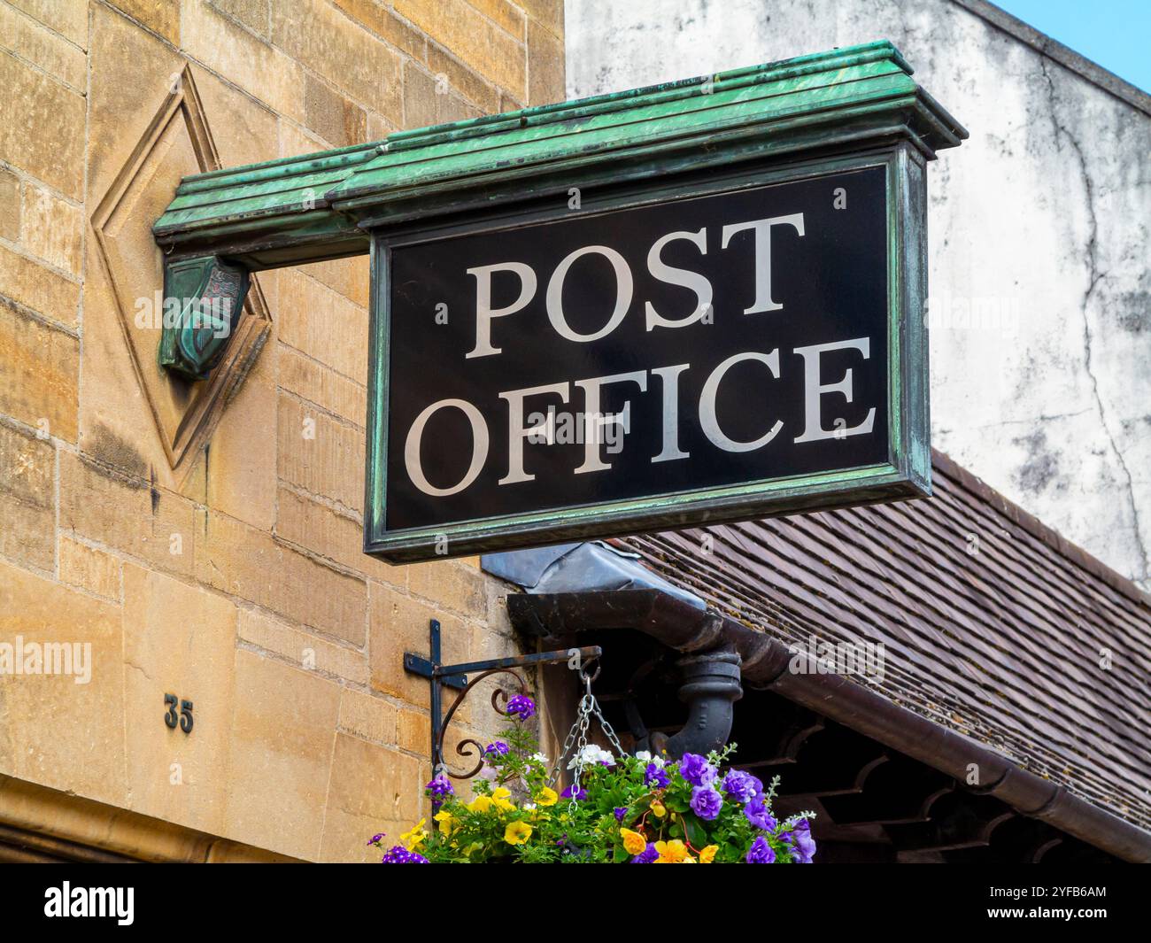 Traditionelles Schild vor einer Postfiliale in Glastonbury Somerset England, Großbritannien, mit Blumen im hängenden Korb unten. Stockfoto