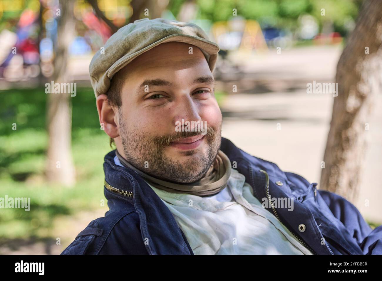 Porträt eines jungen Mannes, der draußen im Park sitzt, freundlich lächelt und auf die Kamera blickt. Stockfoto